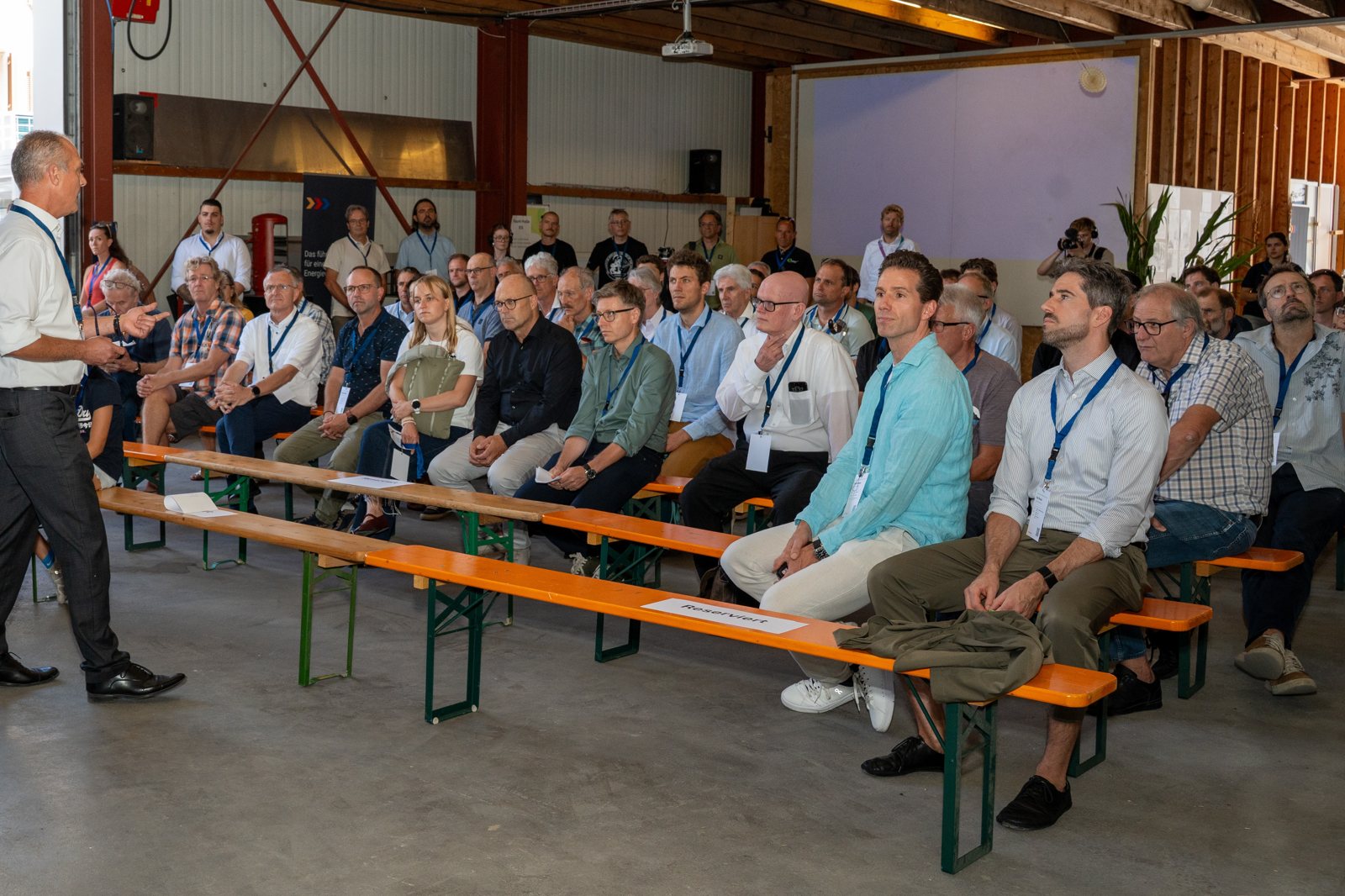 Publikum auf Bierbänken in der Halle des Energieparks Grischa, Frank Schürch davor